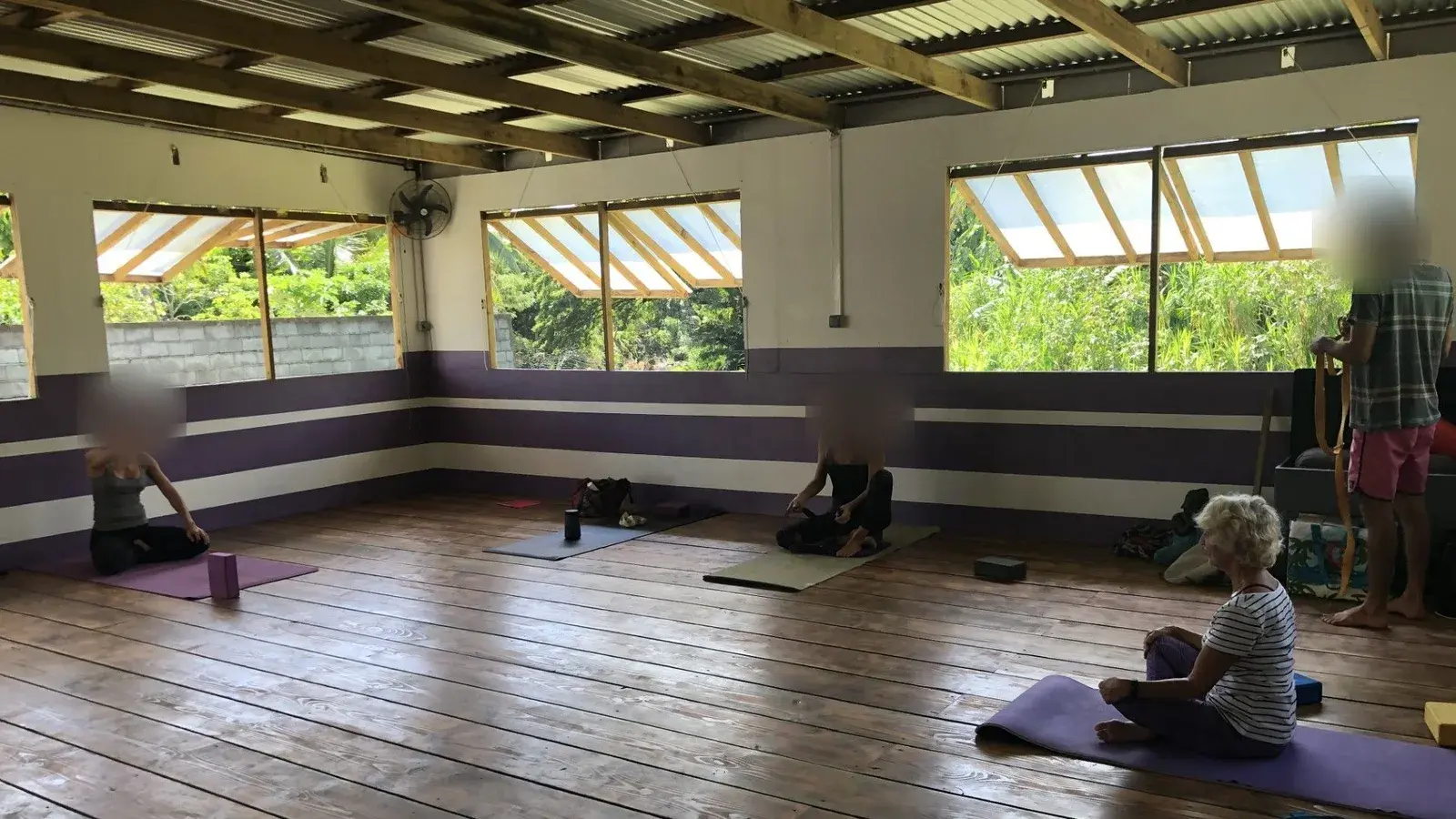 La salle du studio pendant un cours : plancher de bois, murs à bandes violettes et larges fenêtres.